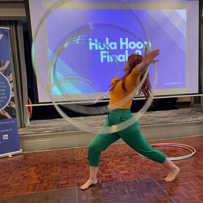 Woman wearing a yellow top and green trousers spinning multiple hula hoops on their arms