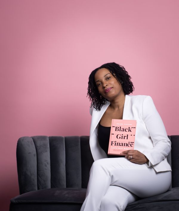 Woman in a white suit sat on a sofa in front of a pink wall