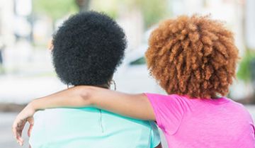 Two women sit closely outside, one with an arm around the other